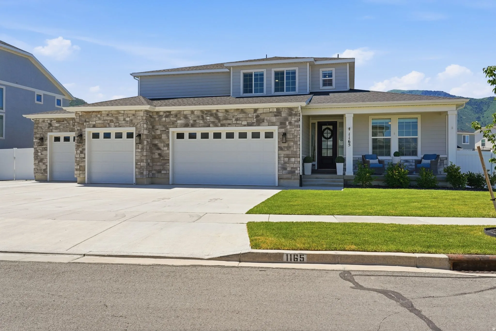 Two-story residence featuring a stone and siding exterior, a covered front porch, and a three-car garage
