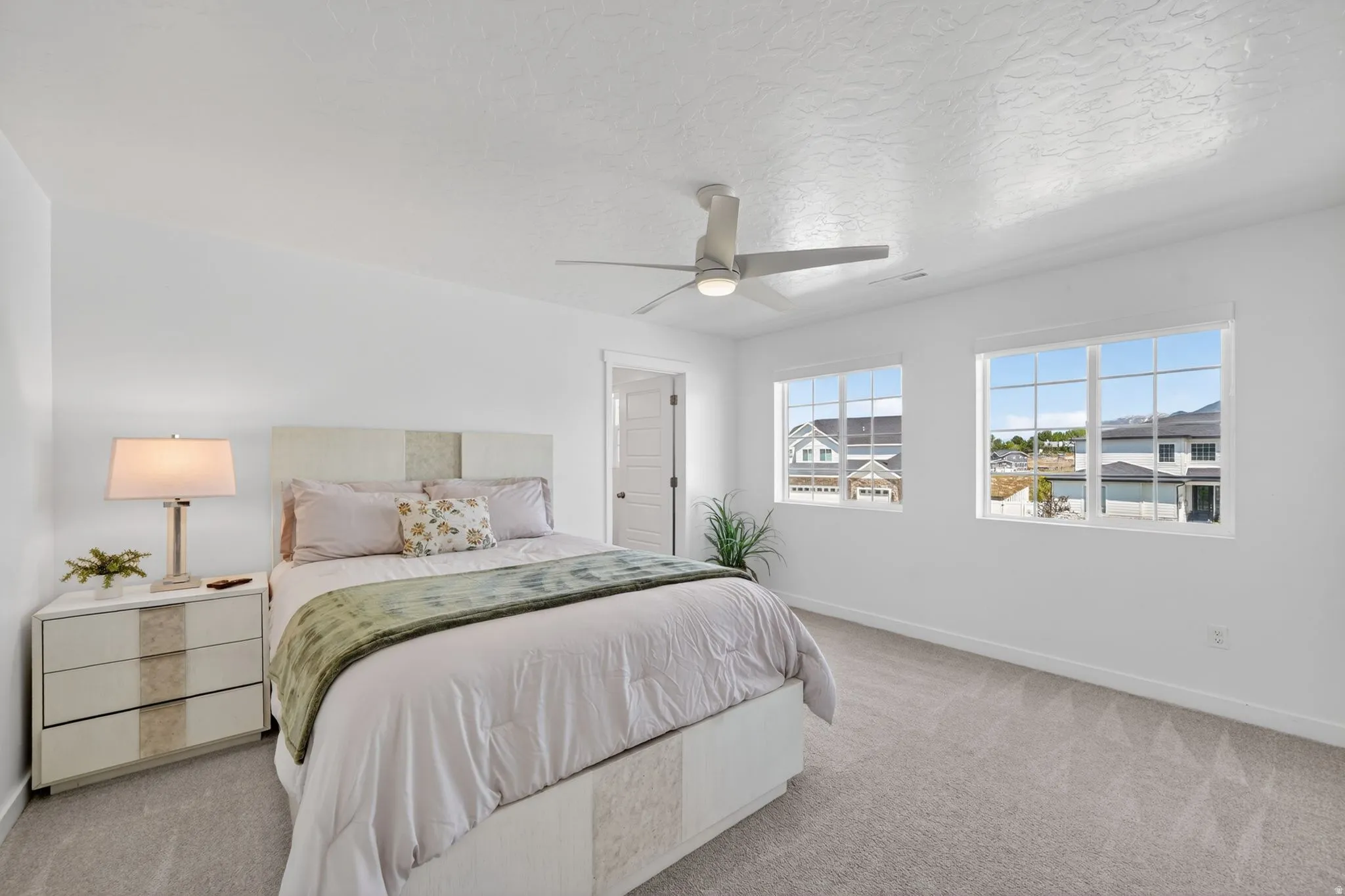 Bright bedroom with two large windows, a ceiling fan, and grey carpet flooring