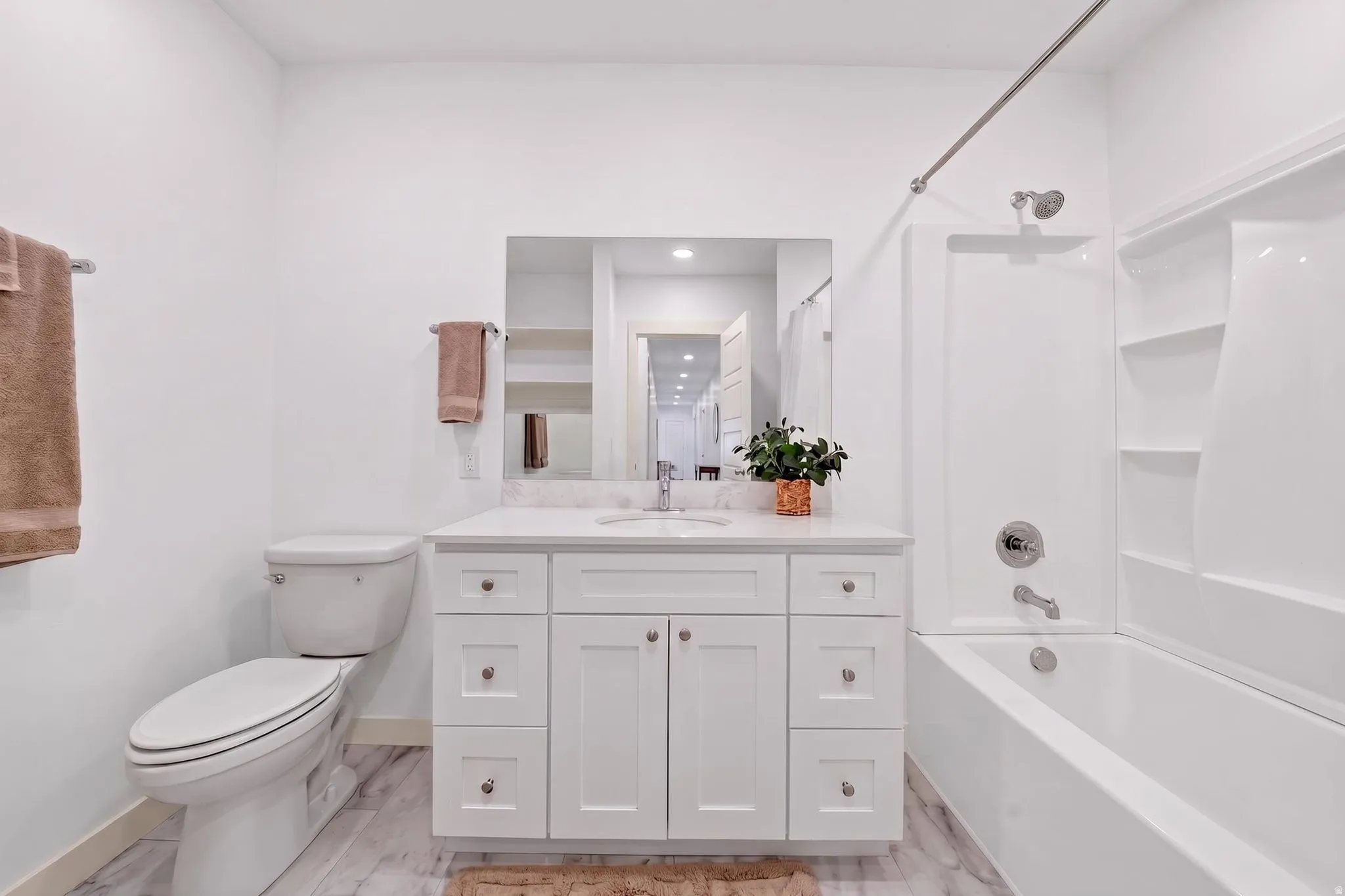 White bathroom featuring a single vanity with a white countertop and undermount sink, a toilet, a tub/shower combination with a white surround, and wood-finish flooring