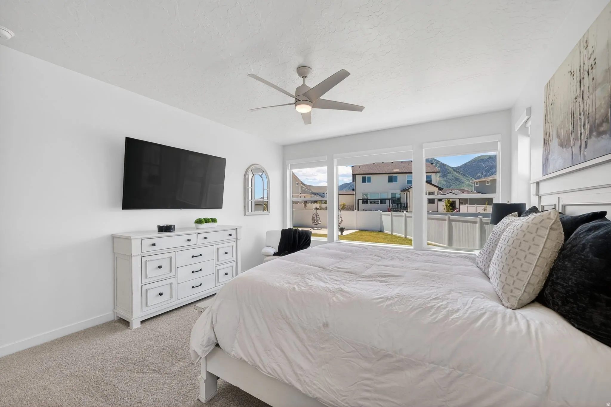 Bright room featuring large windows, a ceiling fan, plush carpeting, and white walls
