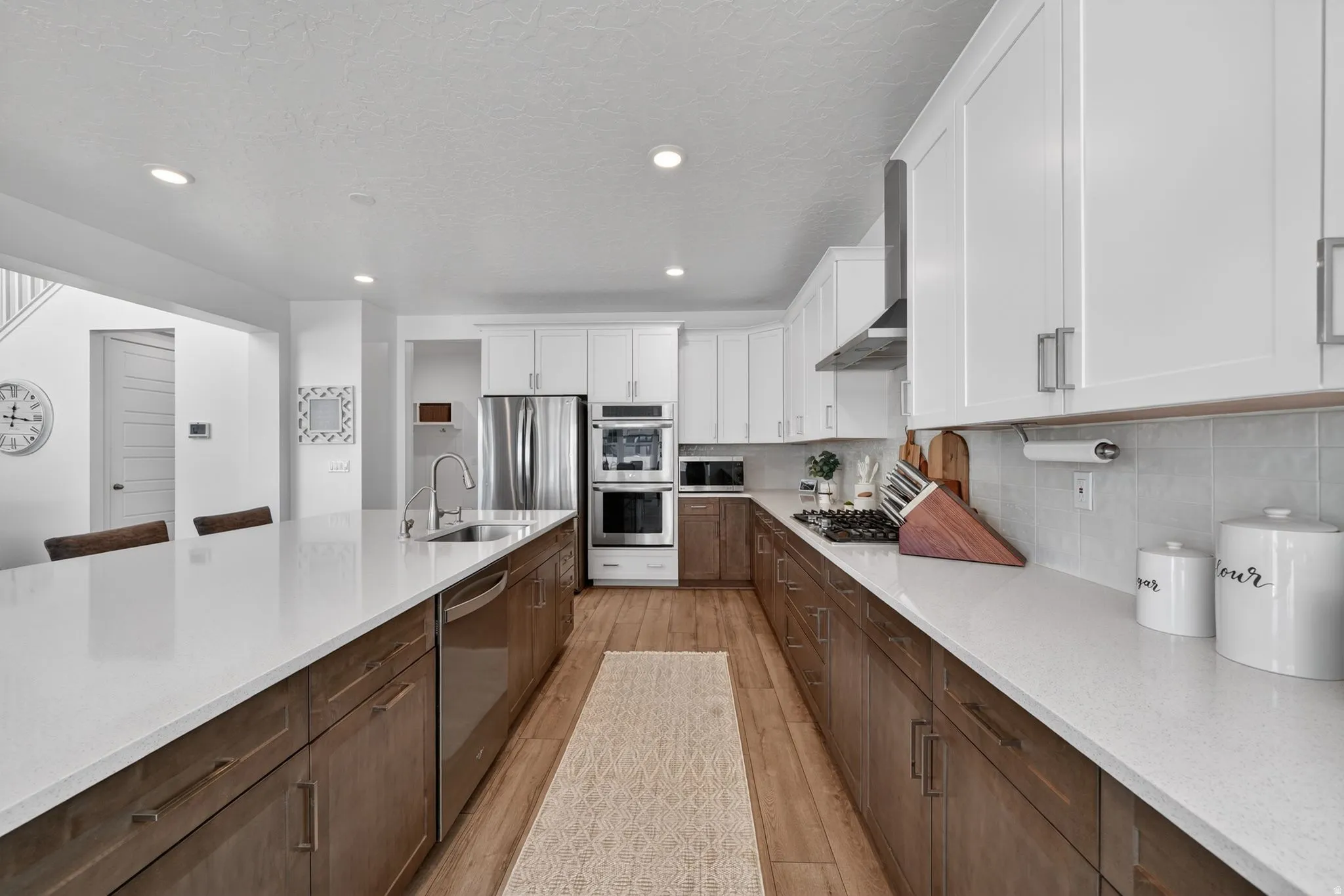 Contemporary kitchen featuring a large island with sink, stainless steel appliances, two-tone cabinetry, light-colored countertops, and wood-finish flooring