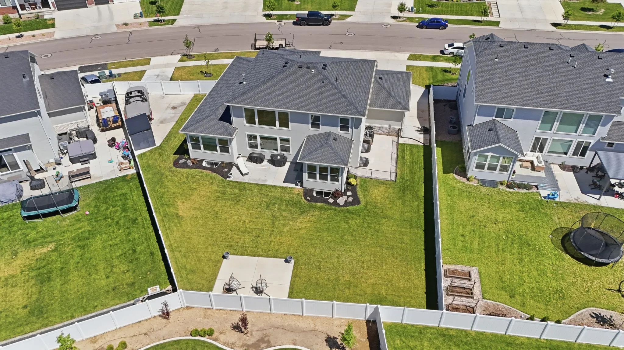 Expansive rear yard featuring a large manicured lawn, multiple concrete patio areas, and perimeter fencing