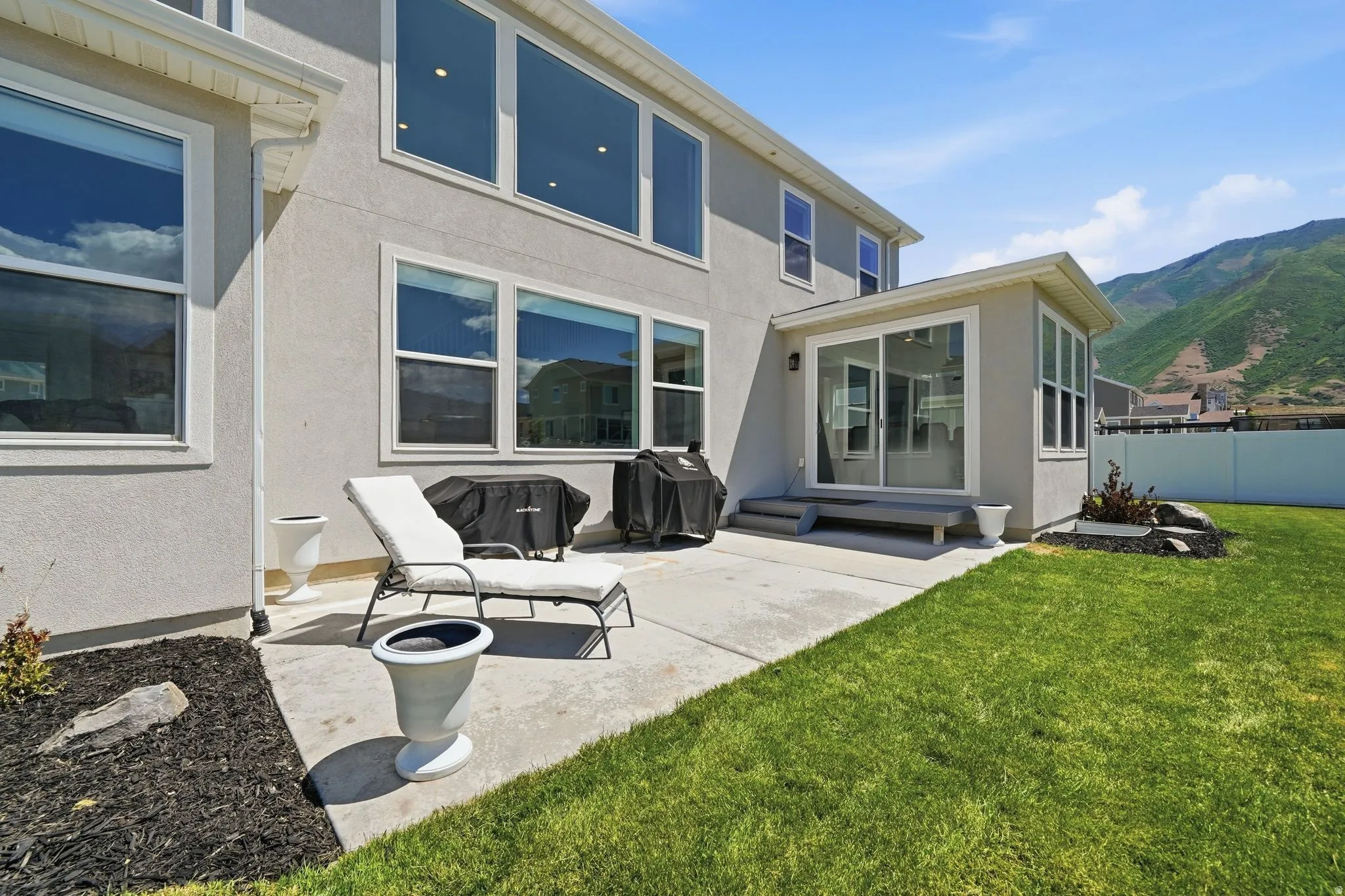 Expansive backyard featuring a manicured lawn, concrete patio, and a sunroom with sliding glass doors