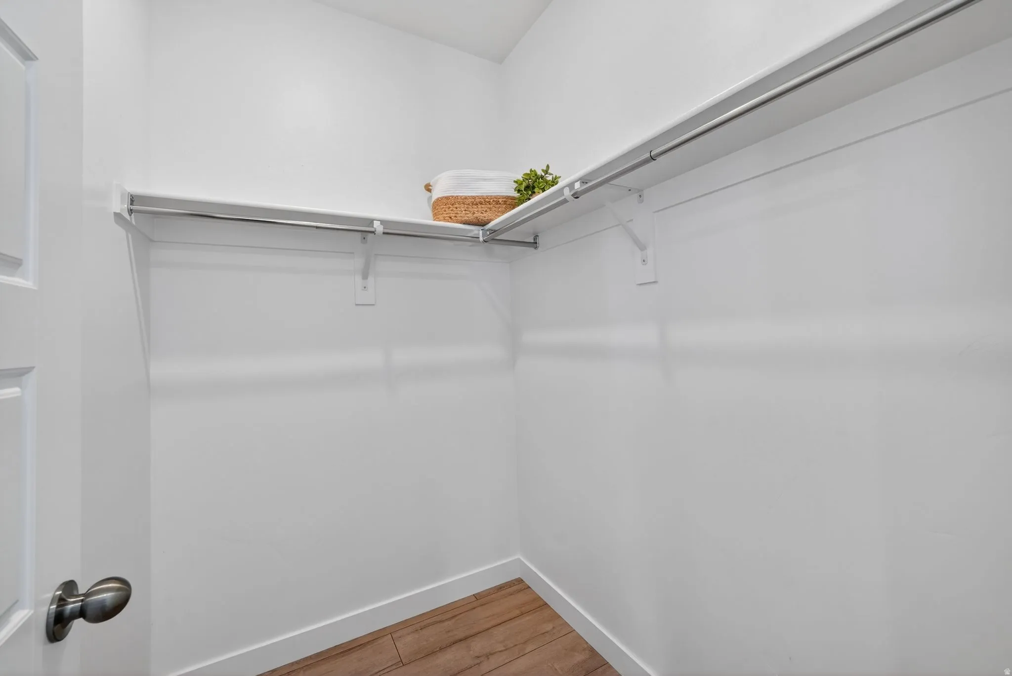 Spacious closet featuring white walls, wood-finish flooring, white baseboards, and built-in white shelving with hanging rods
