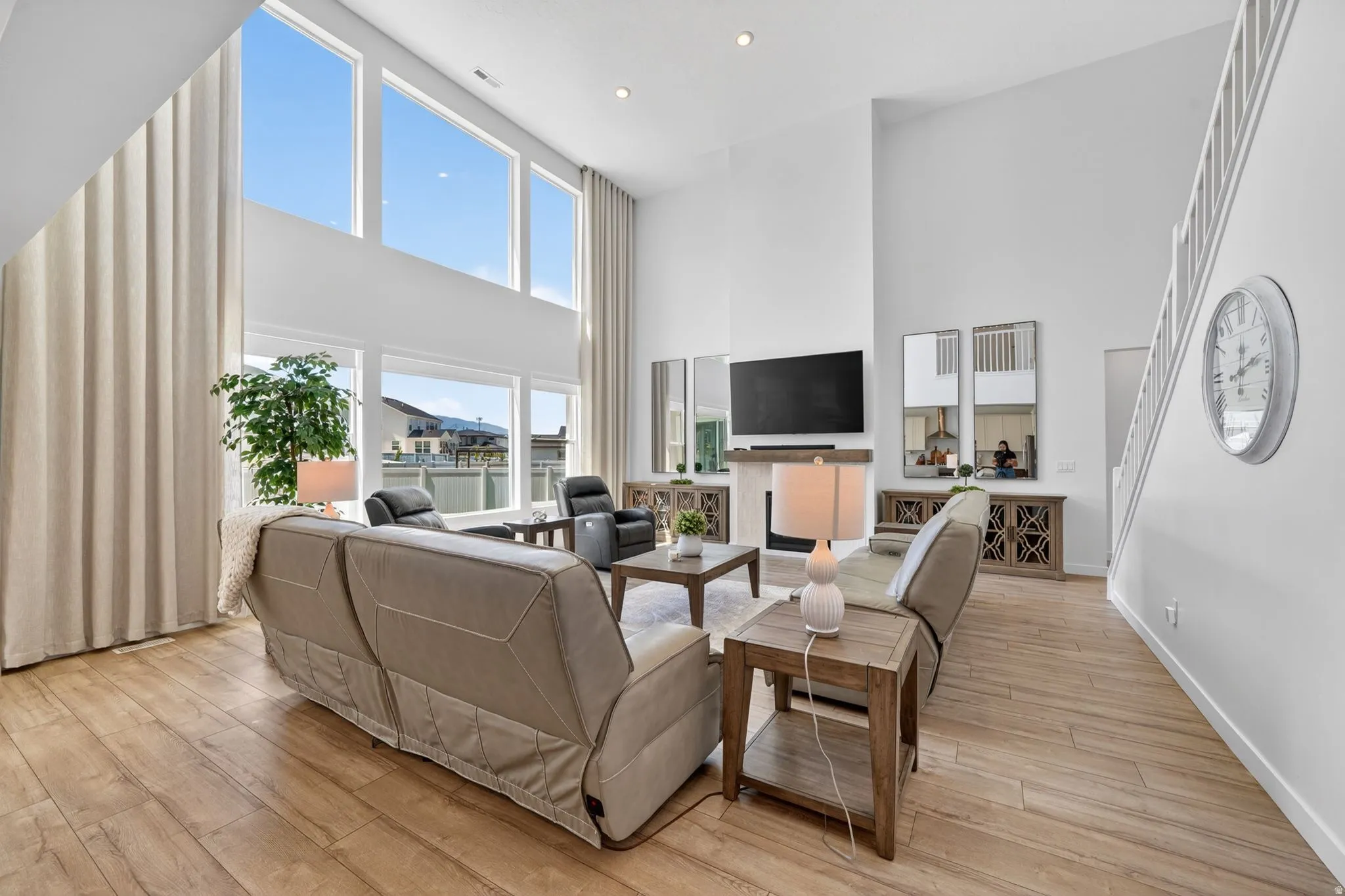 Vaulted ceiling living room featuring wood-finish flooring, a wall of multi-pane windows, a fireplace with a mantel, and an open staircase with white risers and handrails