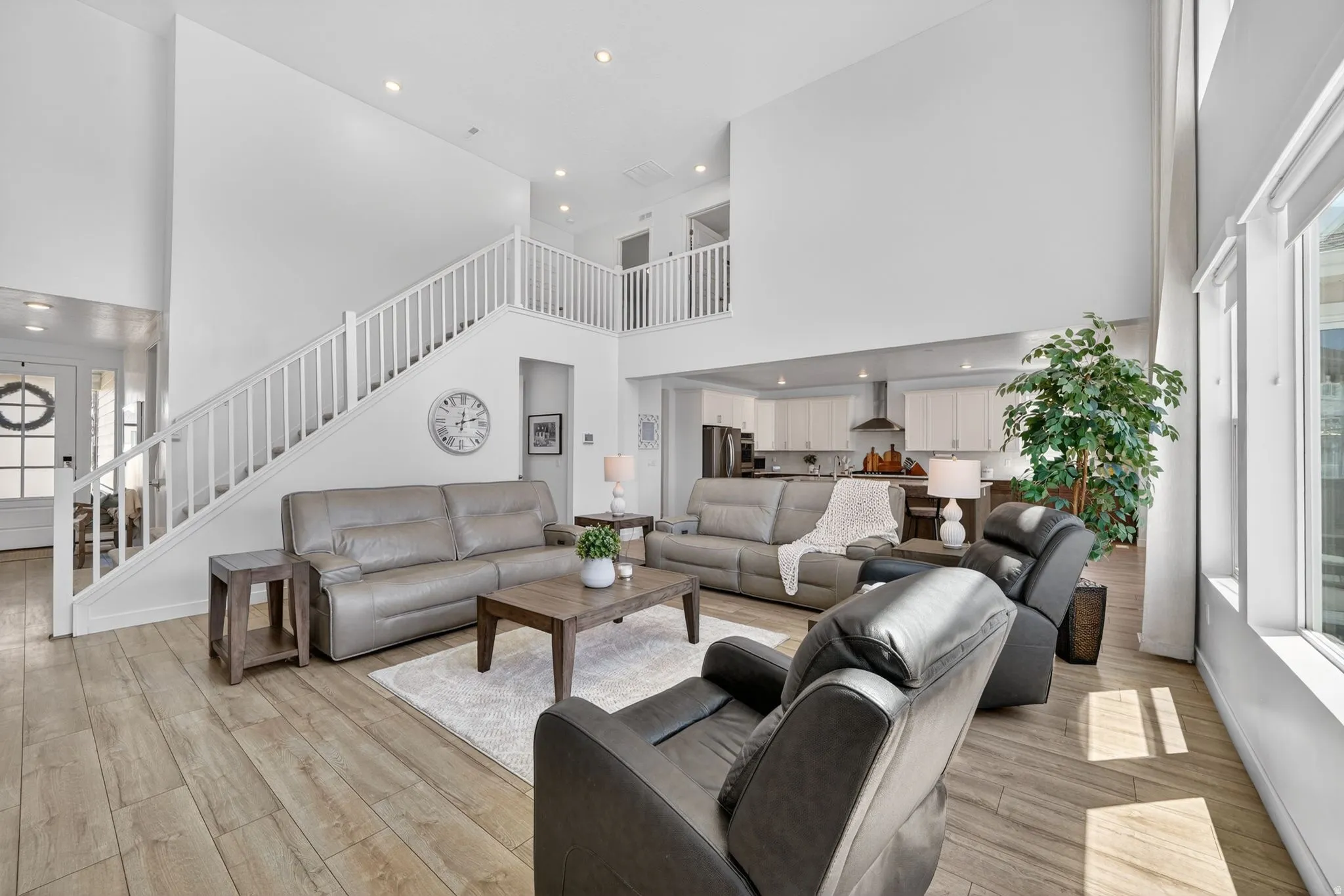 Spacious living room featuring high ceilings, wood-finish flooring, recessed lighting, and a prominent staircase with white railings