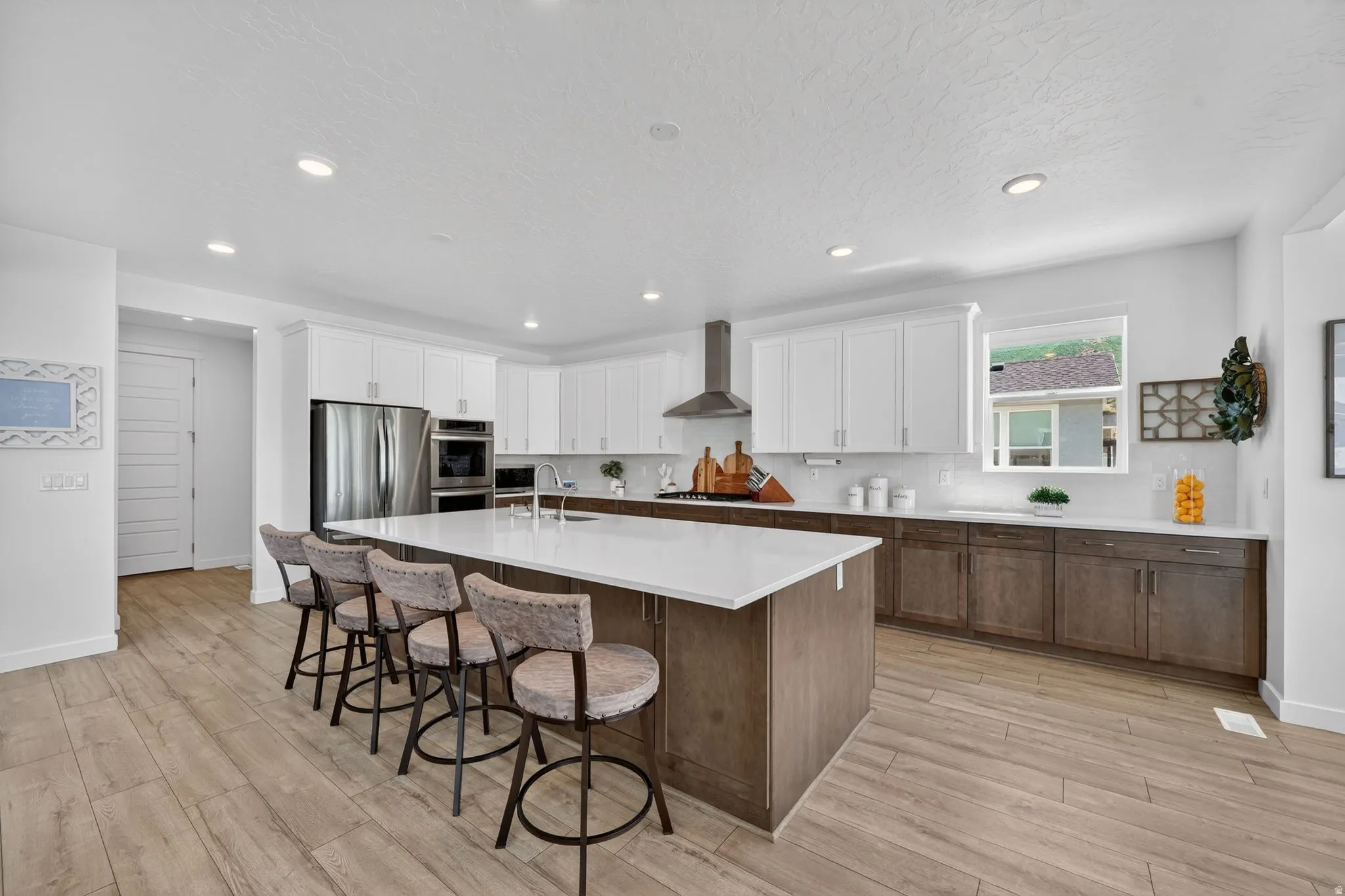 Modern kitchen featuring a large central island with seating, stainless steel appliances, upper white cabinetry, lower wood-finish cabinetry, and wood-finish flooring