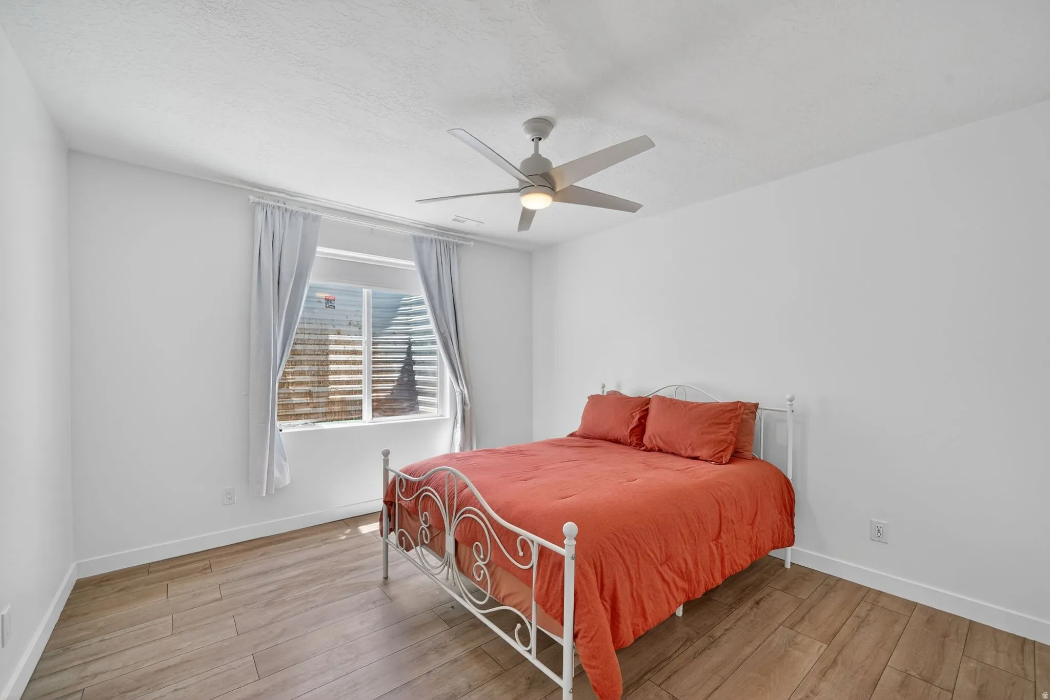 Bedroom featuring wood-finish flooring, a ceiling fan with integrated lighting, a single window, white walls, and white baseboards