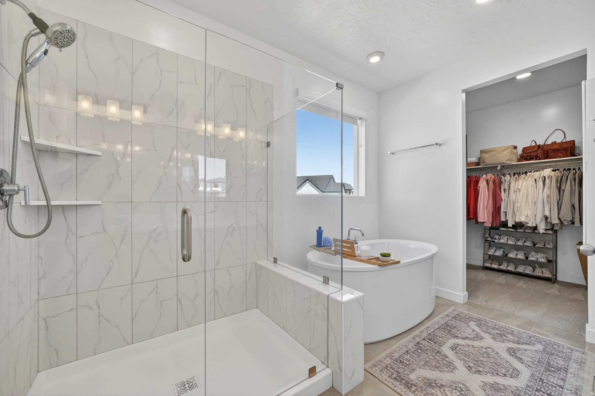 Spacious bath featuring a glass-enclosed shower with subway tile surround, a deep soaking tub, and an adjacent walk-in closet with built-in shelving