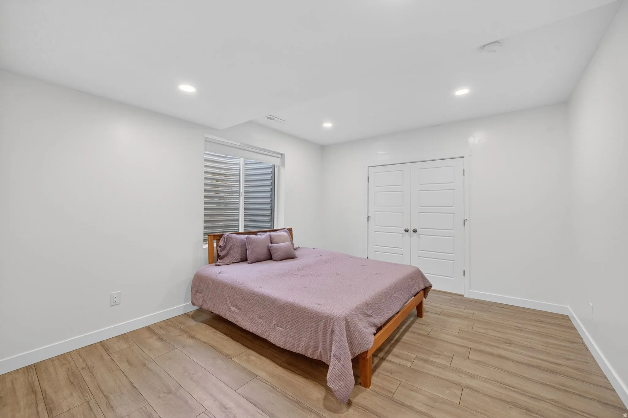 Spacious room featuring wood-finish flooring, recessed lighting, a window with horizontal blinds, and a double-door closet with paneling