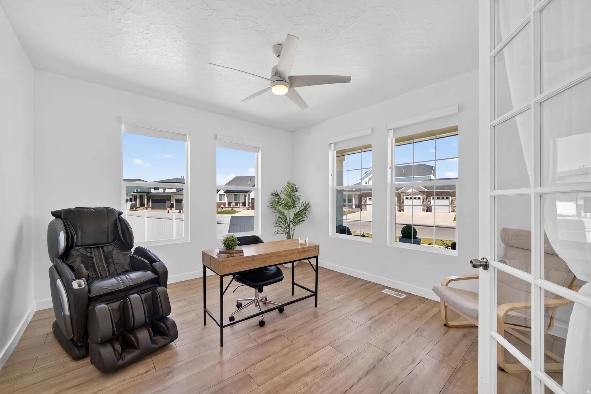 Room featuring wood-finish flooring, a contemporary ceiling fan with integrated lighting, and multiple windows with white trim