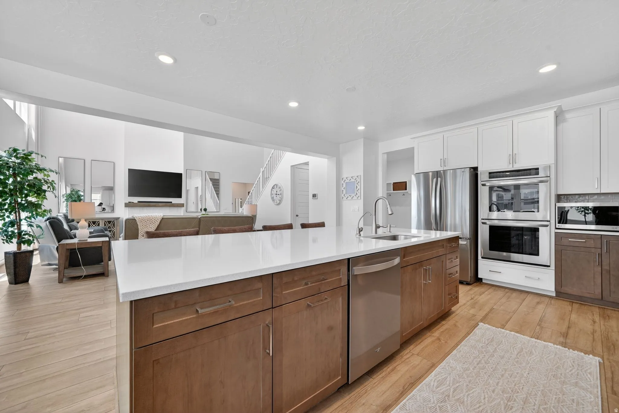 Gourmet kitchen featuring a large island with white countertop, stainless steel appliances, two-tone cabinetry, and wood-finish flooring