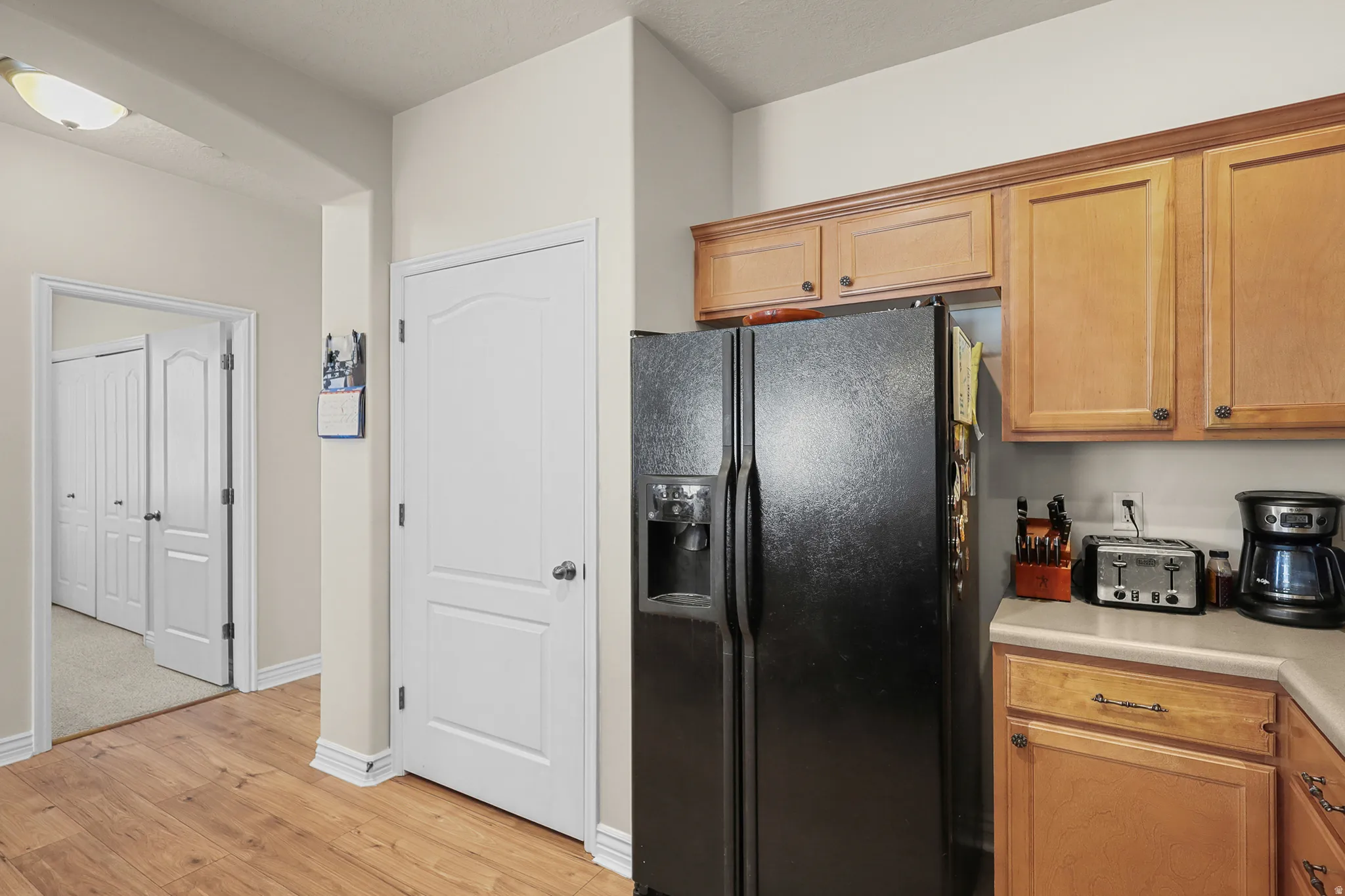 Kitchen area featuring wood-finish flooring, light cabinetry with dark hardware, and a black side-by-side refrigerator