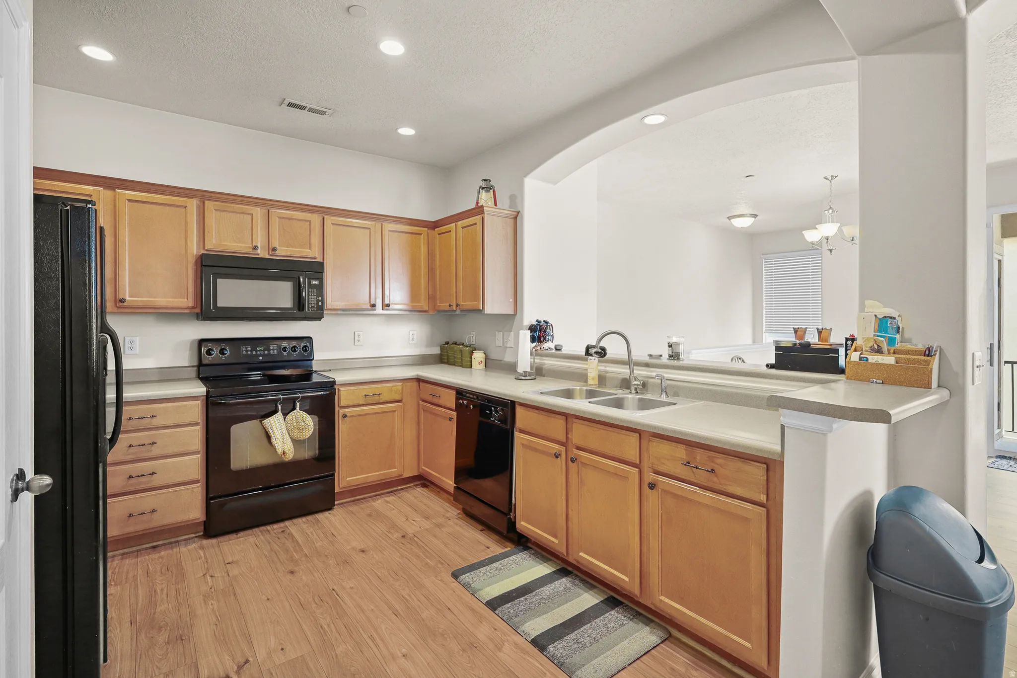 Kitchen featuring wood-finish flooring, a black appliance suite, light-toned countertops, and wood cabinetry