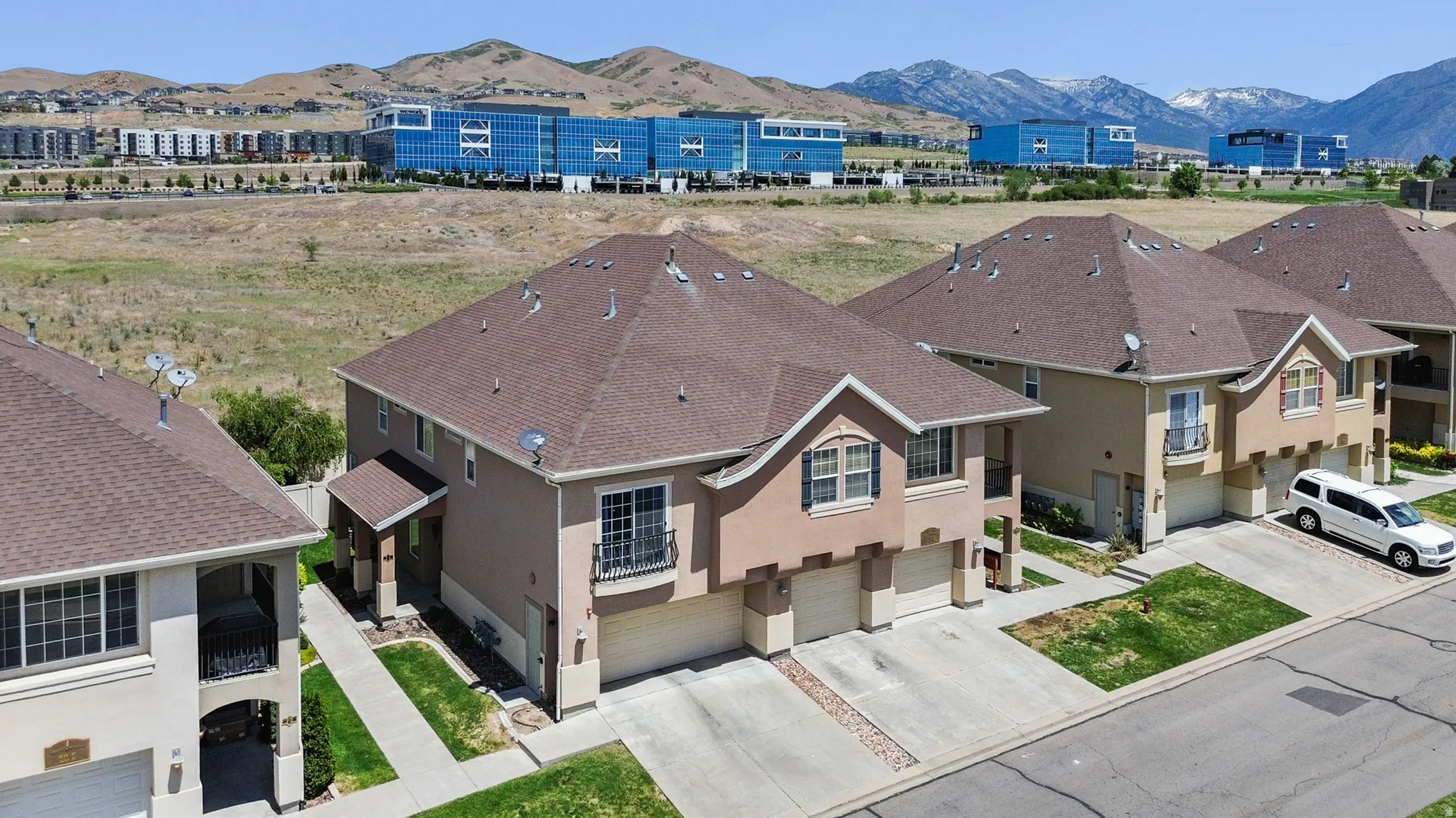 Townhome property featuring a brown shingle roof, tan stucco exterior, and attached garages