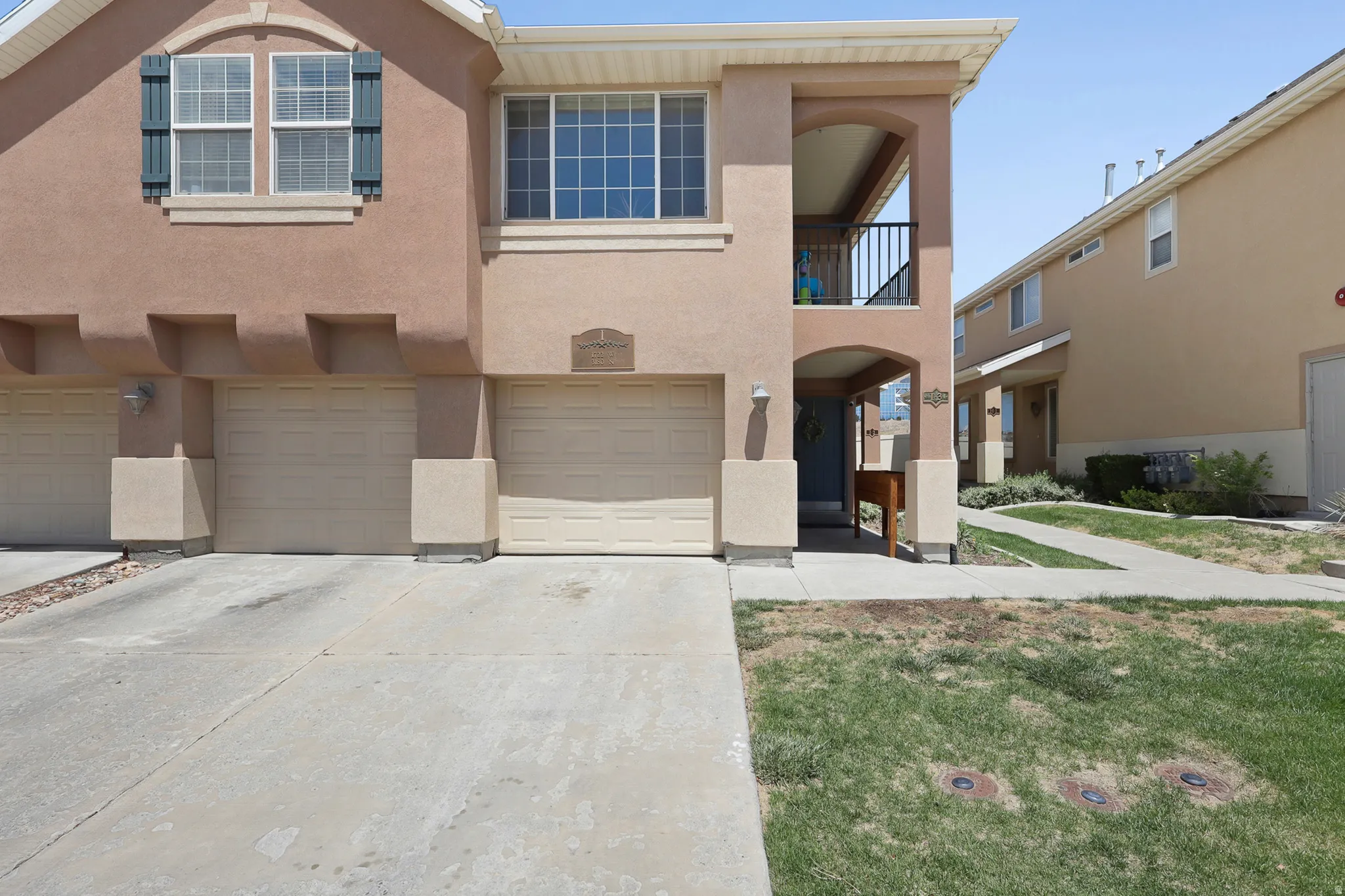 Stucco exterior with two garage doors and an upper-level balcony featuring black iron railing