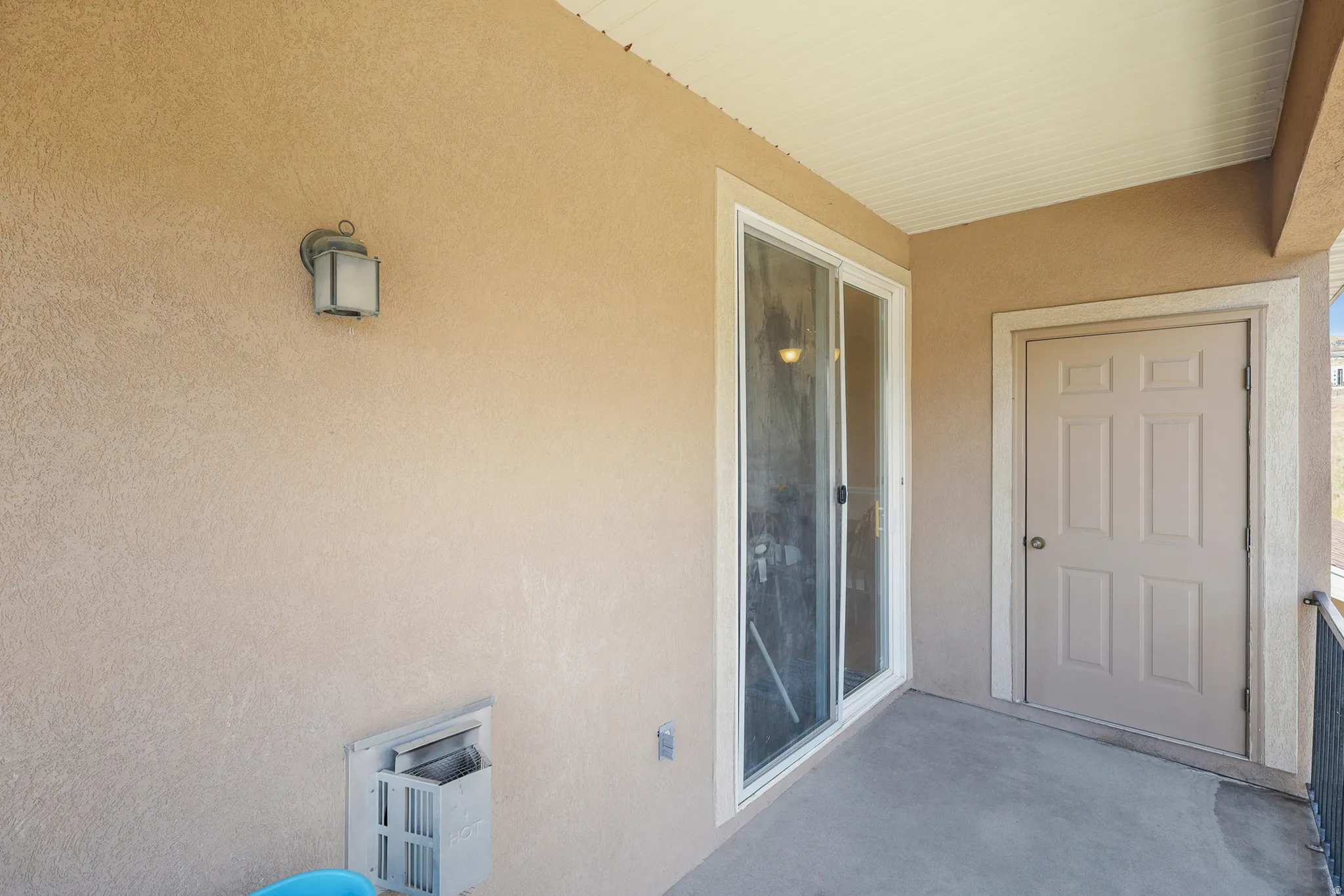 Outdoor patio featuring a stucco exterior, sliding glass door, six-panel exterior door, and a wall-mounted light fixture