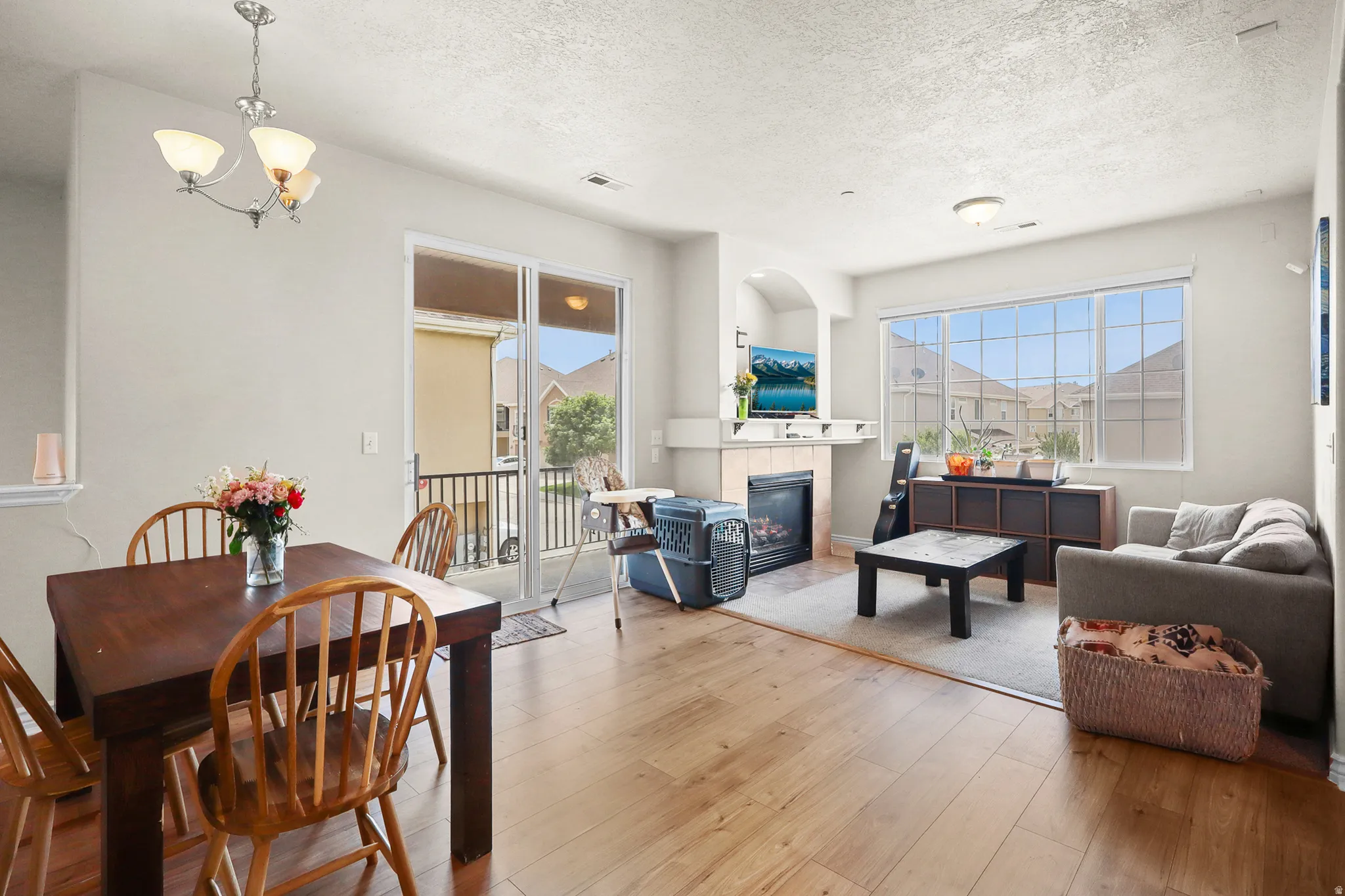 Open-concept living space with wood-finish flooring, a contemporary fireplace with a tiled surround, and large windows providing ample natural light