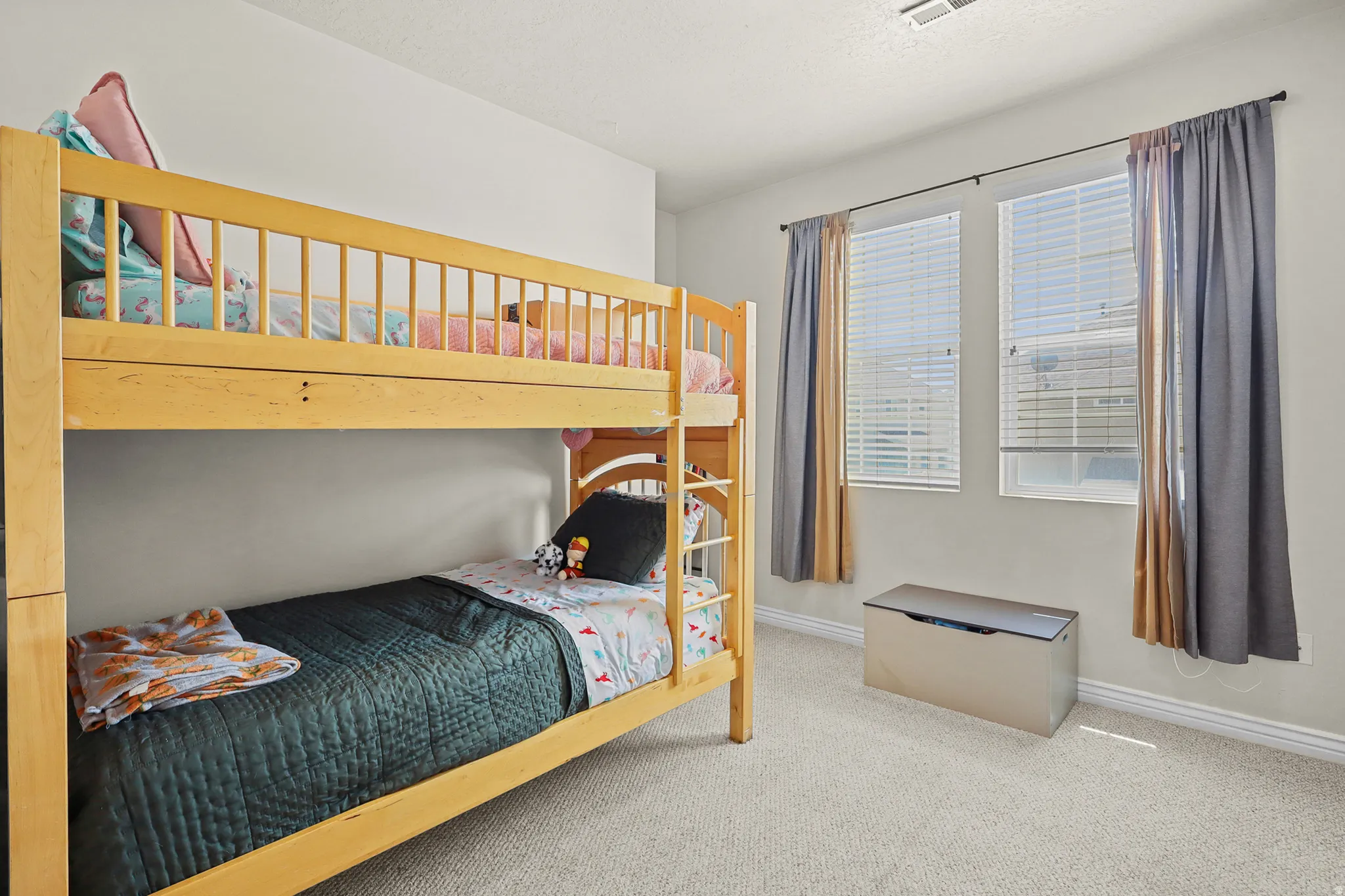 Carpeted bedroom featuring two windows with horizontal blinds and drapery rods