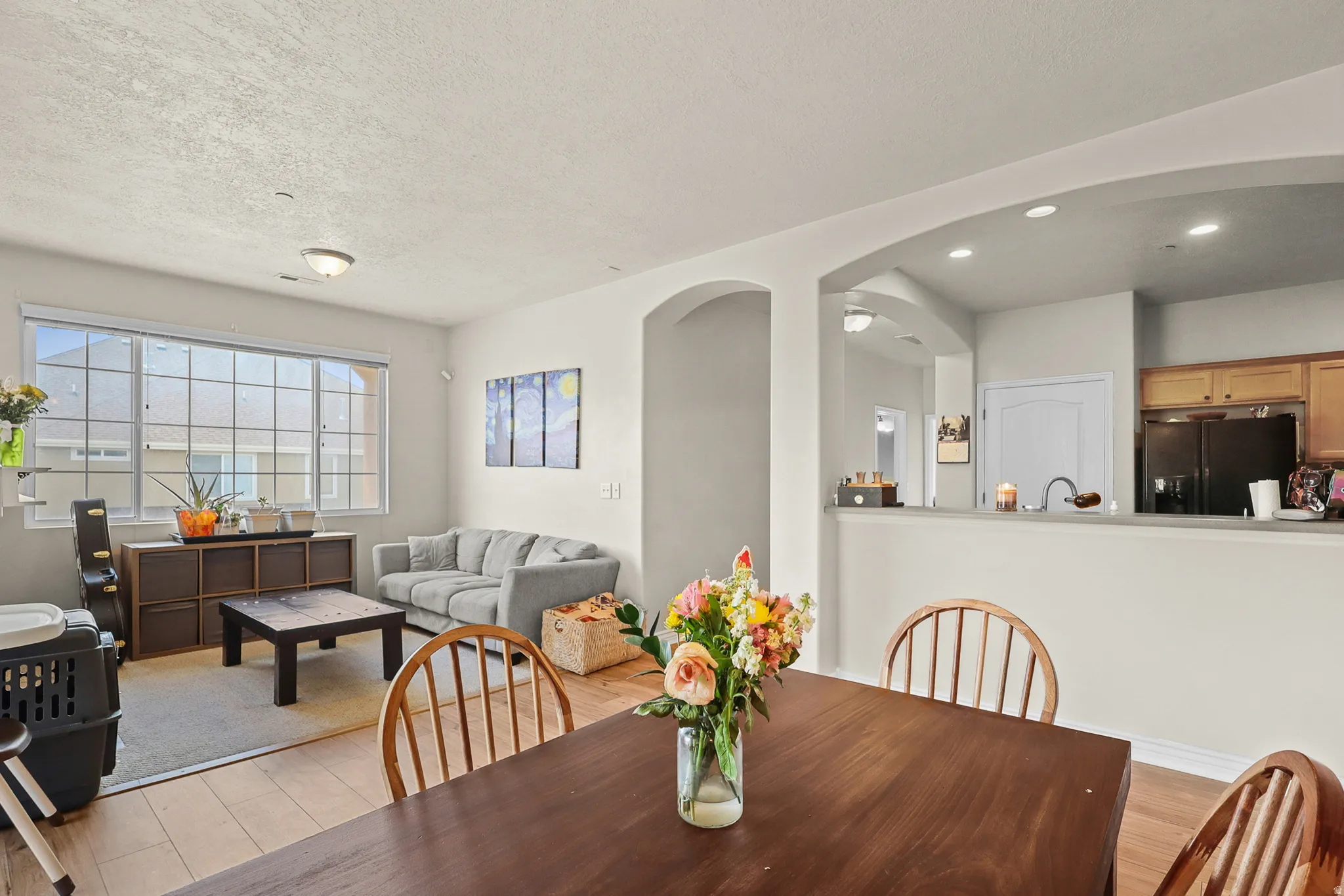Open-concept living space featuring wood-finish flooring, a prominent window with grid panes, and arched doorways