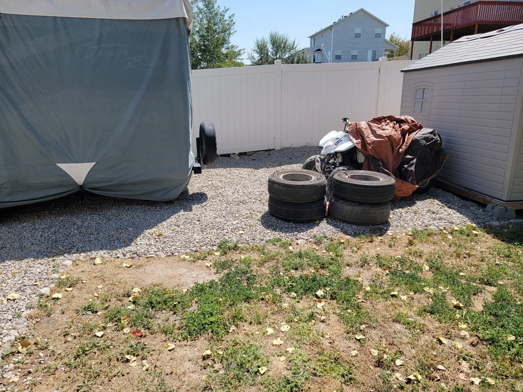 Gravel utility area featuring a storage shed and white privacy fencing