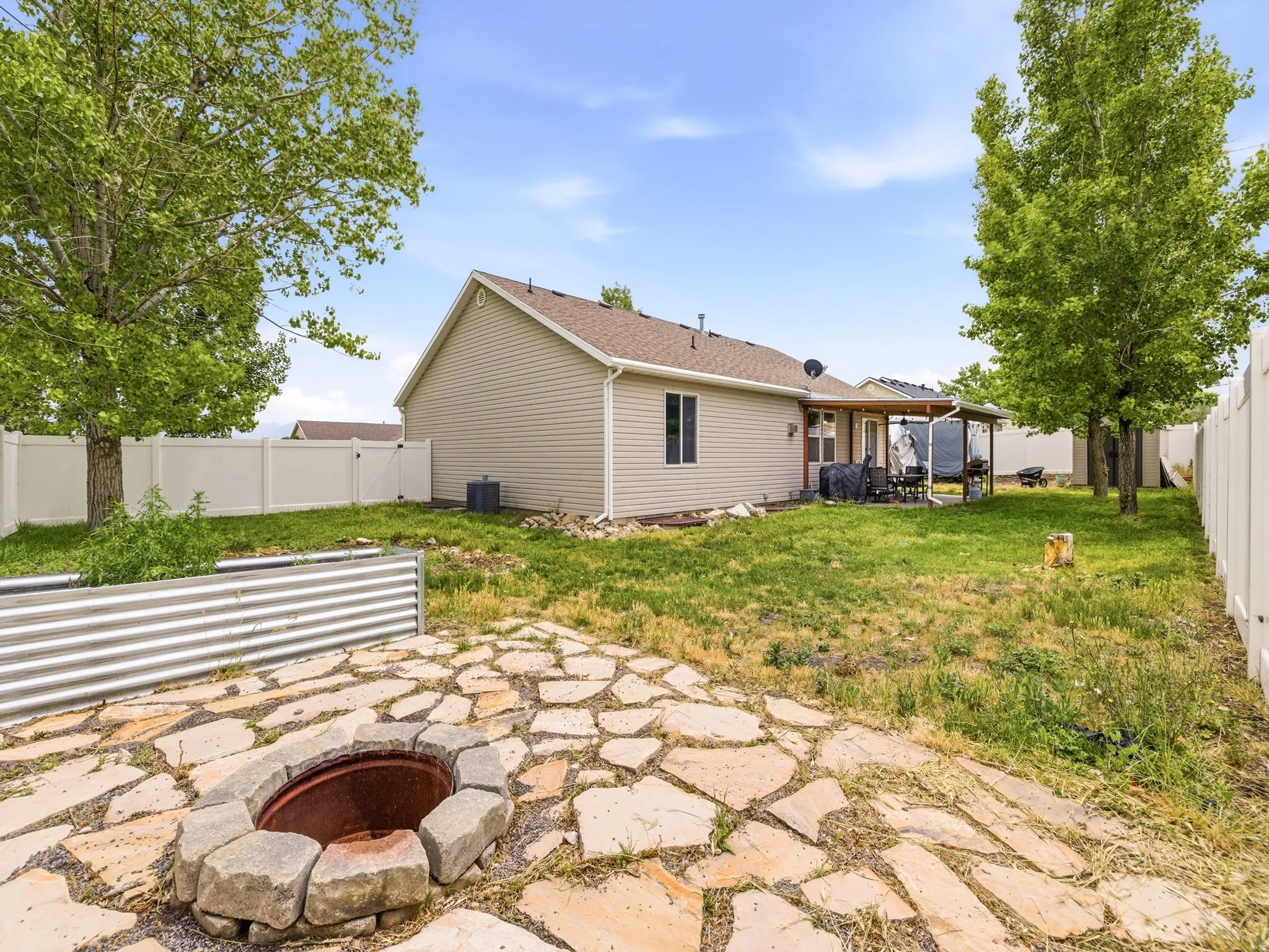 Expansive backyard featuring a stone fire pit, flagstone patio, and a covered back patio