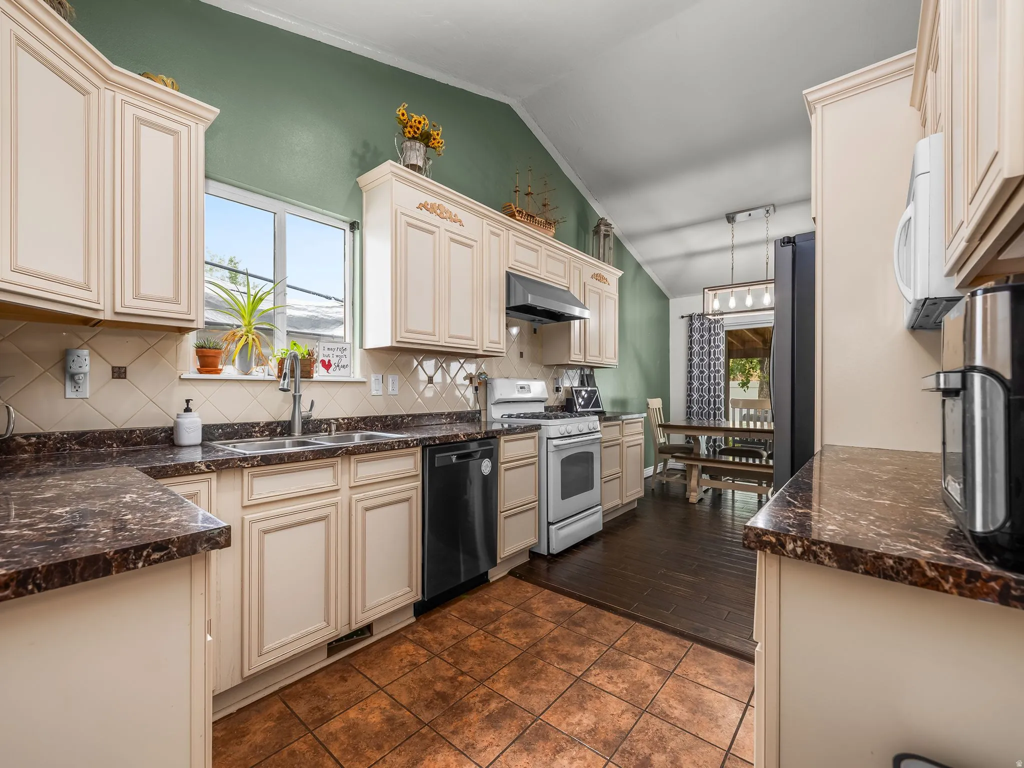 Kitchen featuring a vaulted ceiling with accent wall, recessed window, dark-toned countertops, tile flooring, and cream-colored cabinetry
