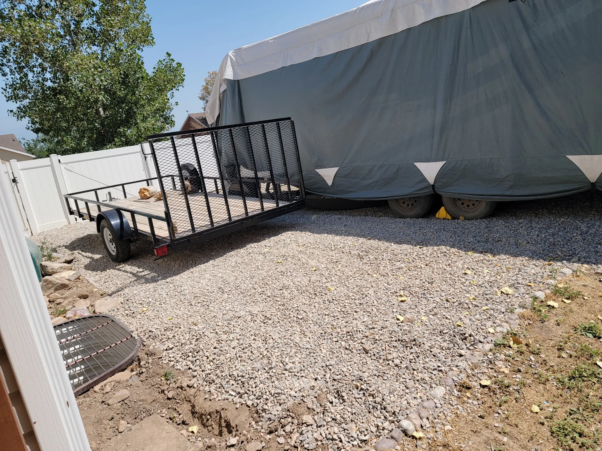 Gravel-surfaced side yard featuring a white vinyl fence and mature trees