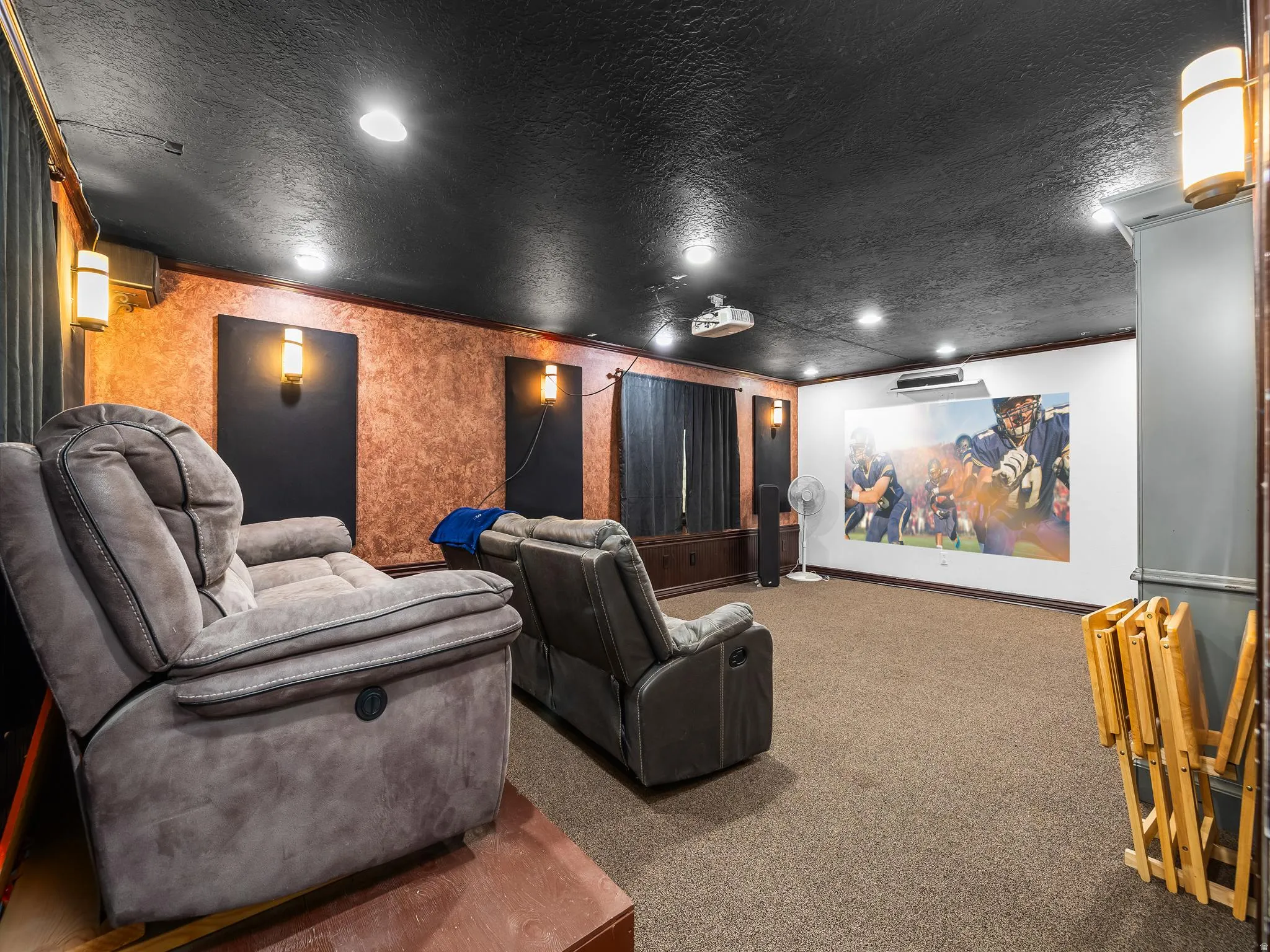 Dedicated media room featuring a large projection screen, recessed lighting, and wall-mounted sconces