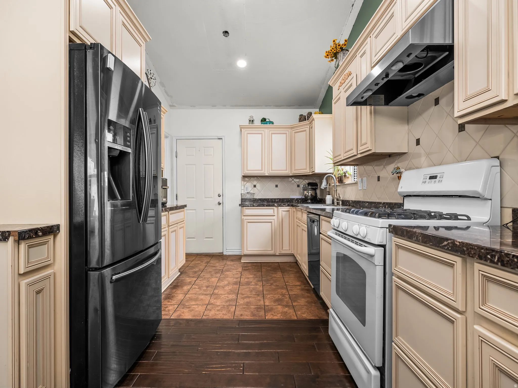 Kitchen featuring cream-colored cabinetry, dark countertops, tile backsplash, and a stainless steel refrigerator