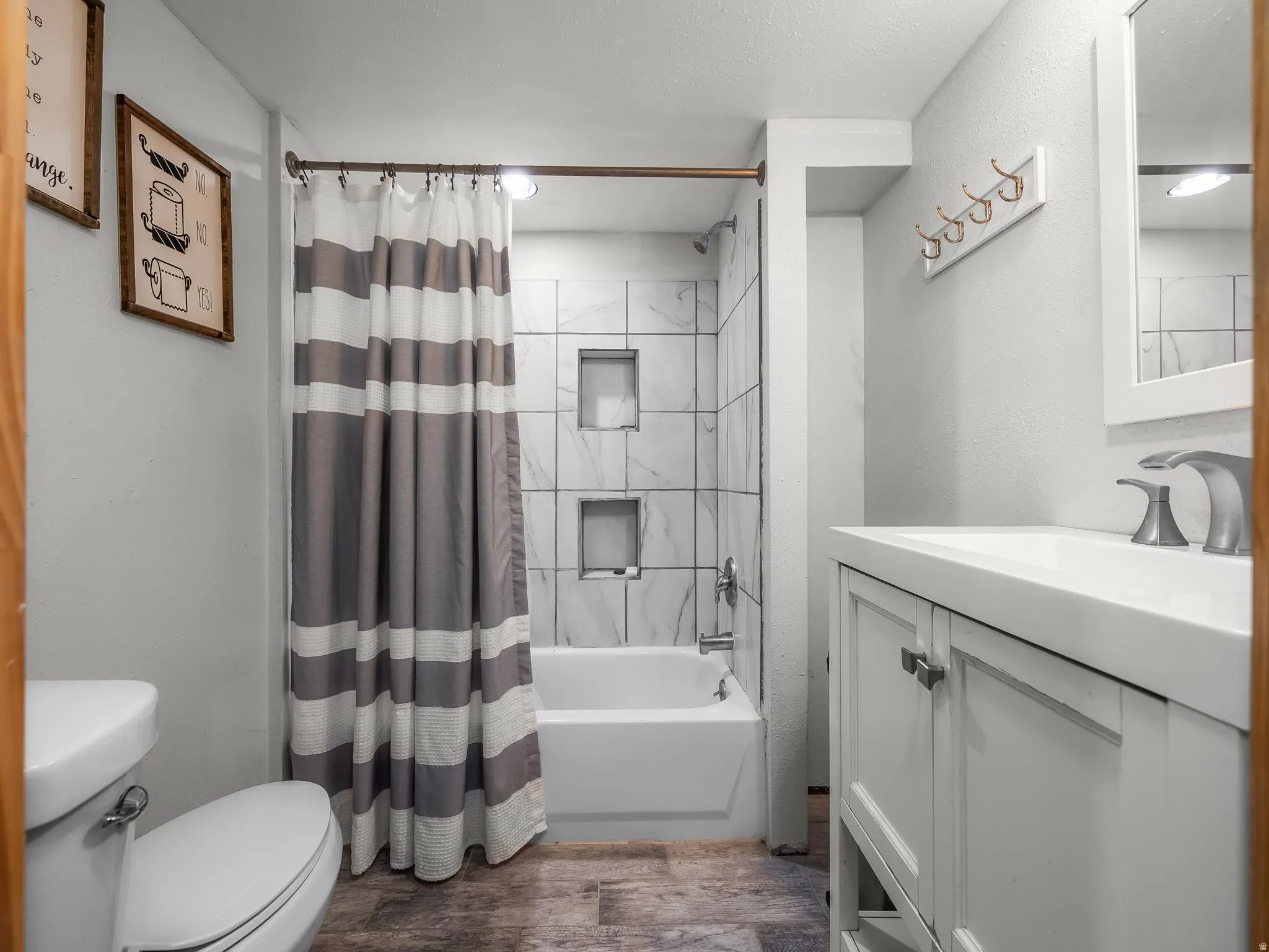 Bathroom featuring a white vanity with integrated sink, a white toilet, and a tiled shower-over-tub with built-in niches