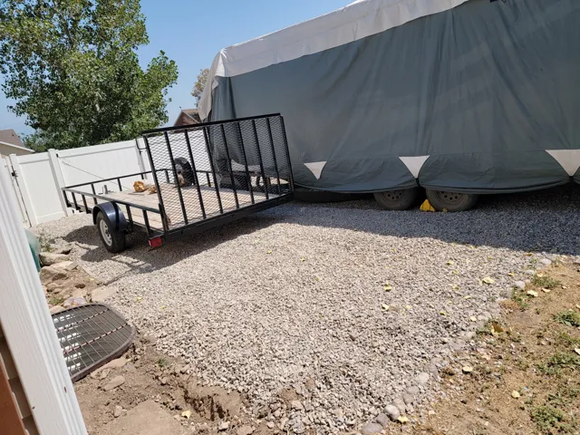 Gravel-surfaced side yard featuring a white vinyl fence and mature trees