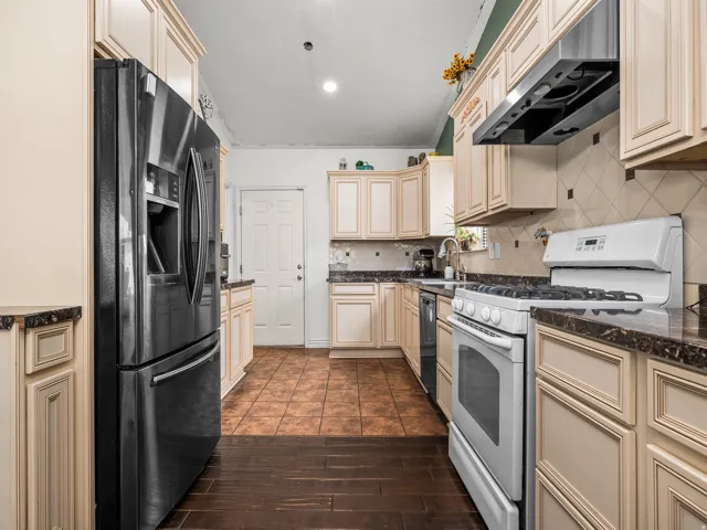 Kitchen featuring cream-colored cabinetry, dark countertops, tile backsplash, and a stainless steel refrigerator