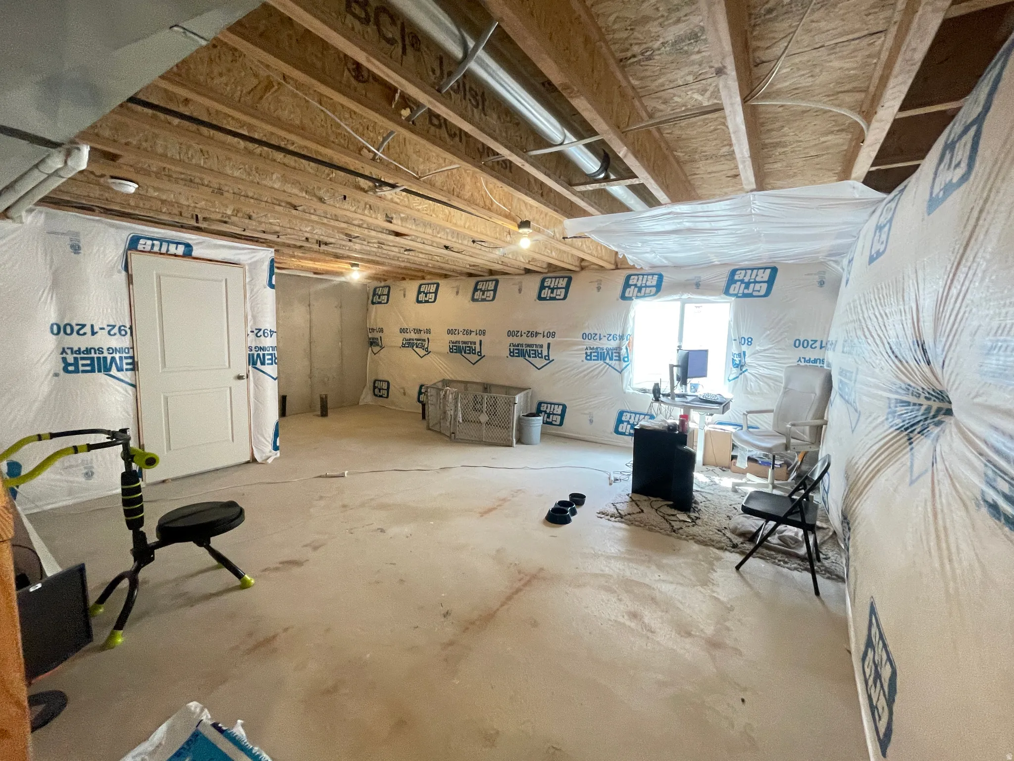 Unfinished basement offering expansive open space, exposed wood joists, a white interior door, perimeter insulation, and a single window
