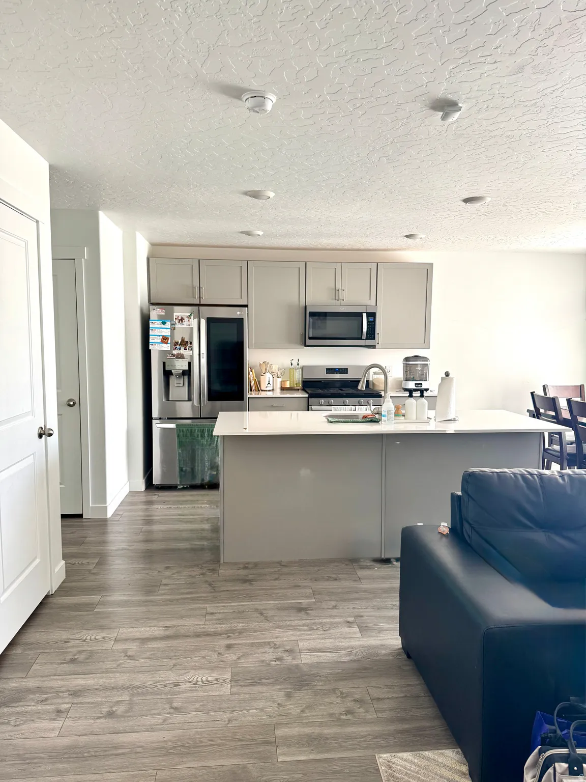Open-concept kitchen featuring gray cabinetry, stainless steel appliances, and a central island with a light-toned countertop