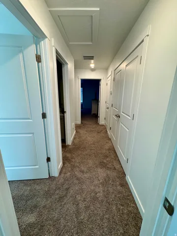 Hallway with brown carpet flooring, white walls, and white trim