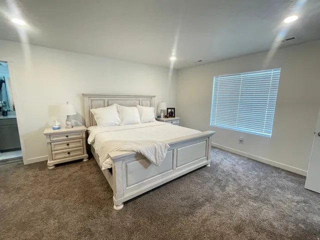 Spacious bedroom featuring plush gray carpeting, recessed lighting, and a large window with horizontal blinds