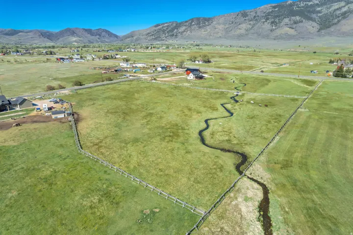 Expansive green acreage featuring a winding creek, perimeter fencing, and distant mountains under a clear sky