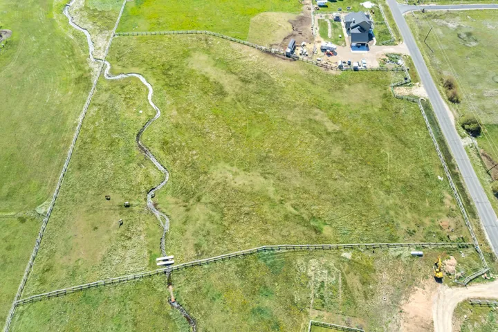 Expansive green acreage featuring a winding creek, perimeter fencing, and road frontage