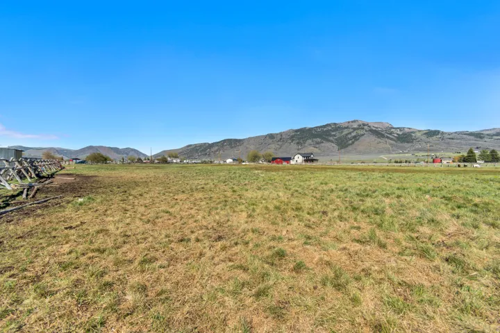 Expansive undeveloped land featuring a wooden fence structure, distant residential properties, and a prominent mountain range backdrop
