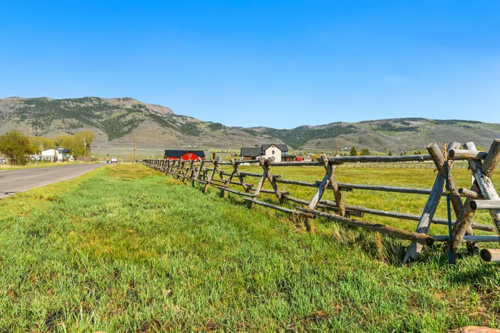 Expansive green field with a rustic split-rail fence under a clear blue sky