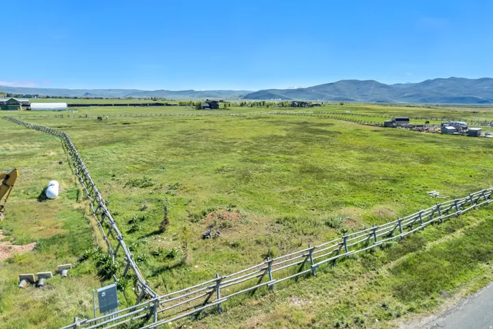 Expansive green fields featuring post-and-rail fencing, distant mountain ranges, and scattered agricultural structures