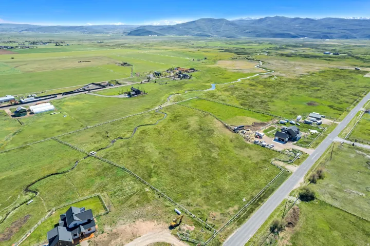 Expansive green landscape featuring a visible creek, mountainous horizon, and road frontage