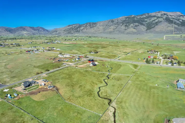 Expansive rural landscape featuring a winding stream, green pastures, and distant mountains