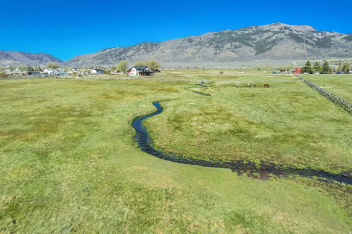 Expansive green pasture with a serpentine waterway and distant mountain range