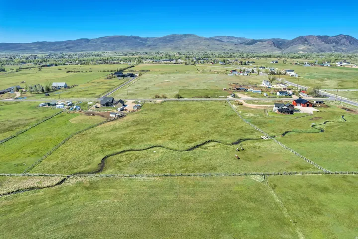 Expansive green pastures featuring a winding stream and distant mountain ranges