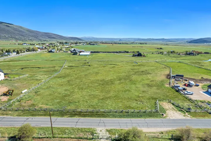 Expansive land parcel featuring a green, grassy field, partial fencing, and direct road frontage