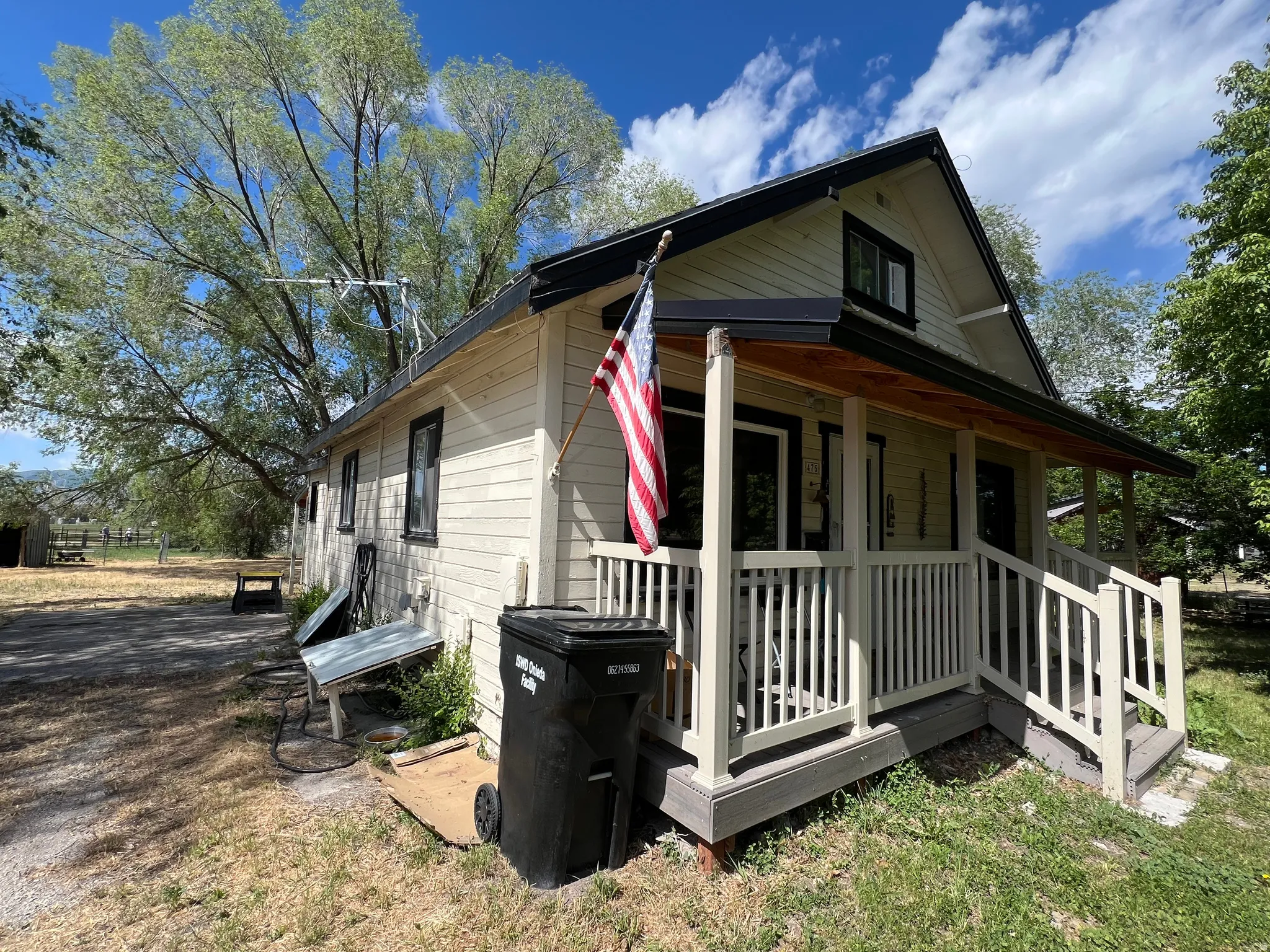 Exterior featuring light-colored siding with dark trim, a covered front porch with white railings, and an exposed wood-finish ceiling on the porch