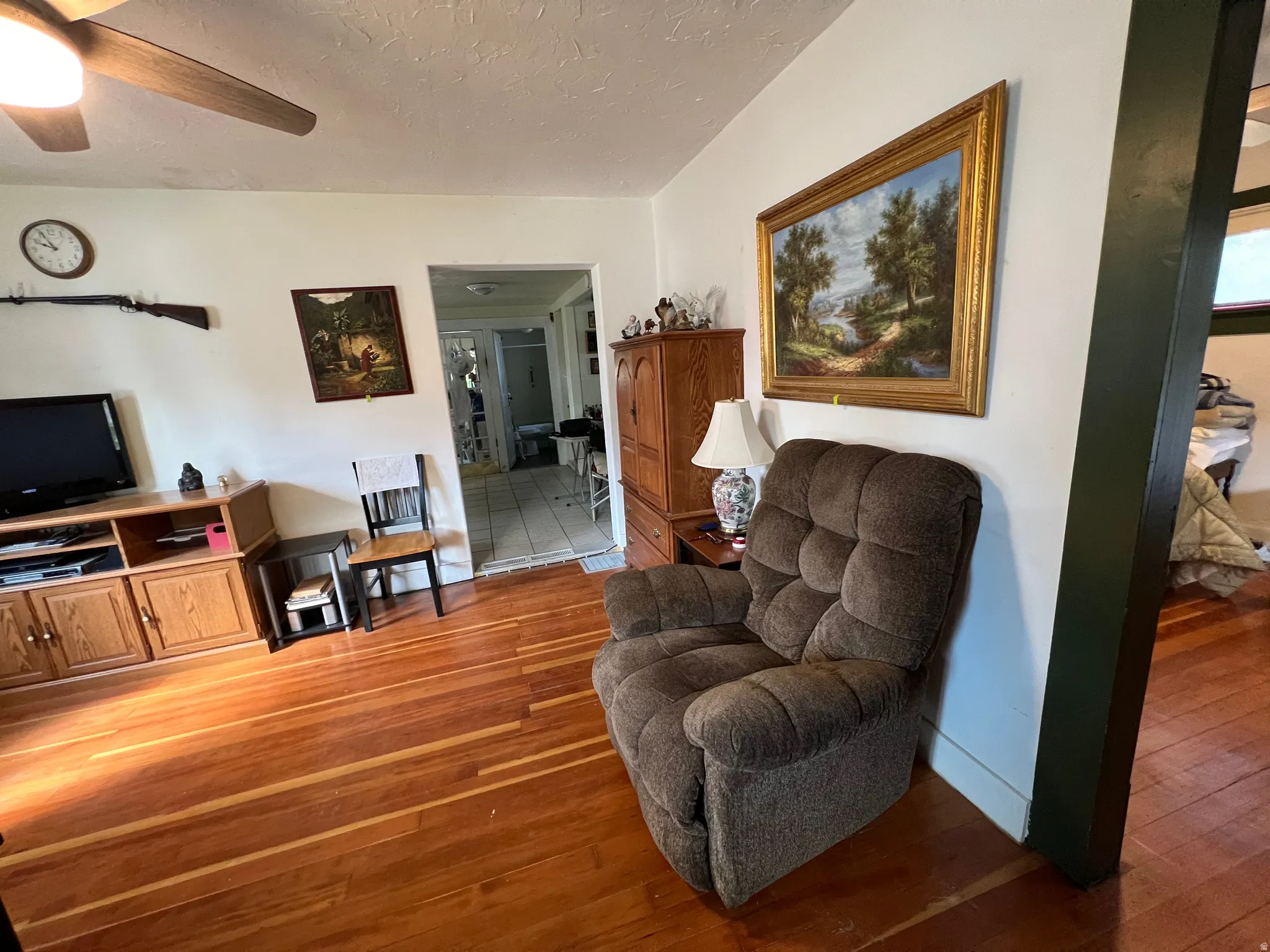 Living area featuring wood-finish flooring, a ceiling fan, and a painted accent beam