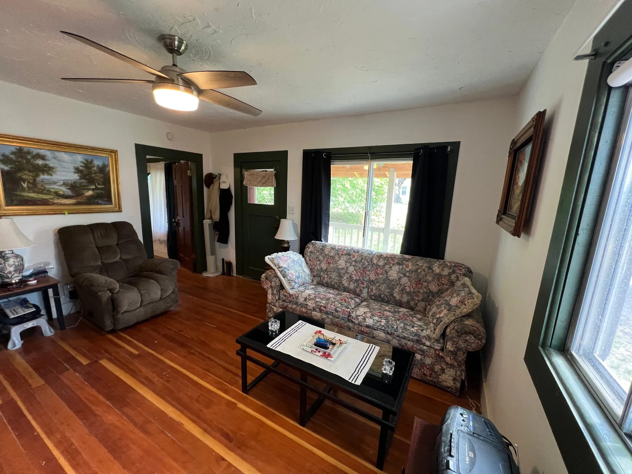 Living area featuring hardwood flooring, a ceiling fan with integrated lighting, and dark trim around windows and doorways